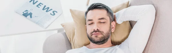 Plan panoramique d'un bel homme barbu les yeux fermés reposant sur un canapé à la maison — Photo de stock