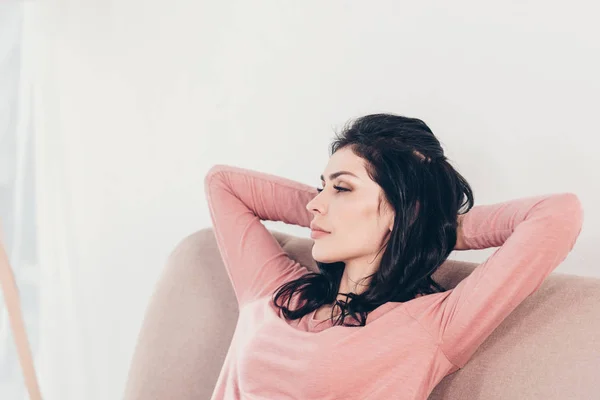 Красива жінка відпочиває на дивані з руками за головою вдома — стокове фото
