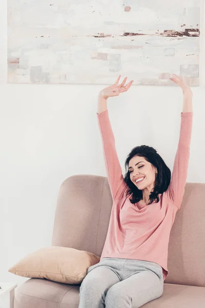 Bella donna sorridente seduta sul divano con le mani tese a casa — Foto stock