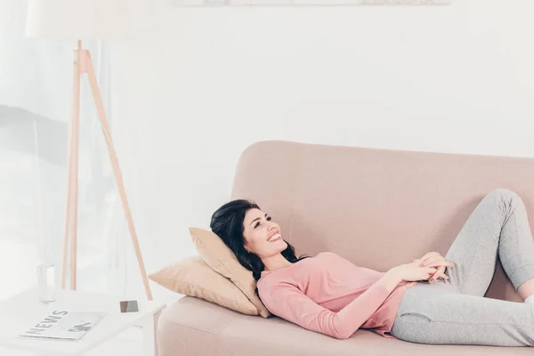 Красива усміхнена жінка відпочиває на дивані вдома у вітальні — стокове фото