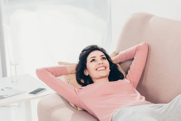 Hermosa mujer feliz descansando en el sofá con las manos detrás de la cabeza en casa - foto de stock