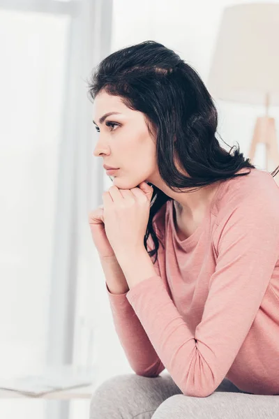 Schöne aufgeregte Frau sitzt und stützt Kinn mit den Händen zu Hause — Stockfoto