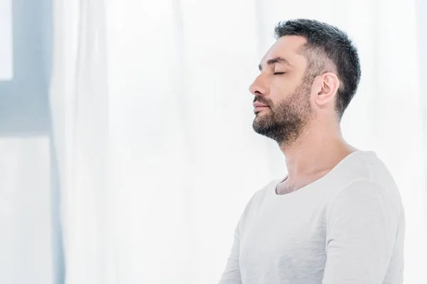 Side view of handsome bearded man with eyes closed at home with sunlight and copy space — Stock Photo