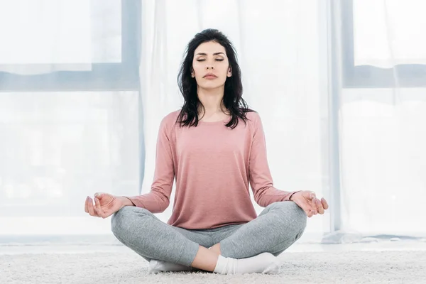 Bela mulher com os olhos fechados em Lotus Pose praticando meditação na sala de estar em casa — Fotografia de Stock