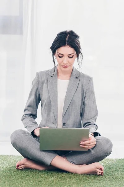 Красива бізнес-леді в костюмі сидить на траві килимок і використовує ноутбук — стокове фото