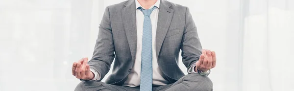 Panoramic shot of businessman in suit meditating in Lotus Pose — Stock Photo