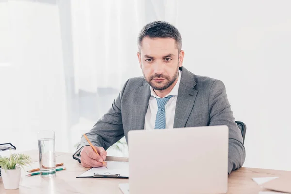 Bel homme d'affaires en costume assis au bureau et utilisant un ordinateur portable au bureau — Photo de stock