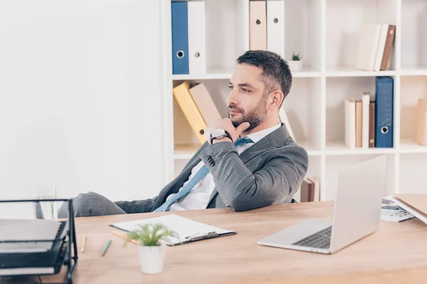 Bell'uomo d'affari pensieroso in giacca e cravatta seduto alla scrivania con laptop in ufficio — Foto stock