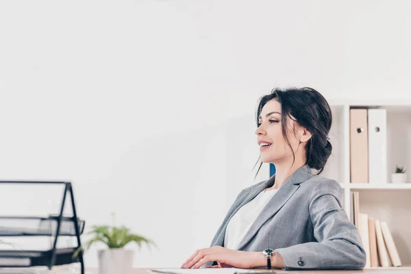 Beautiful businesswoman in suit sitting in office with copy space — Stock Photo