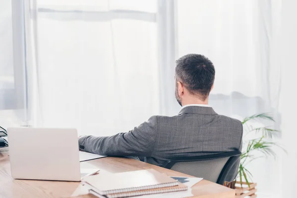 Back view of businessman sitting at table with laptop in office — Stock Photo