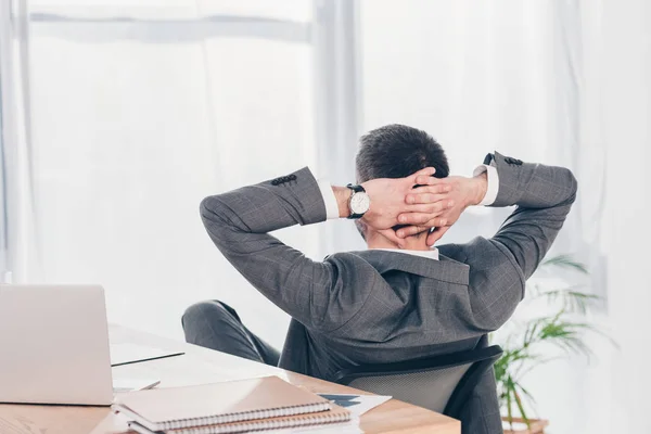 Vue arrière de l'homme d'affaires avec les mains derrière le dos assis à la table dans le bureau — Photo de stock