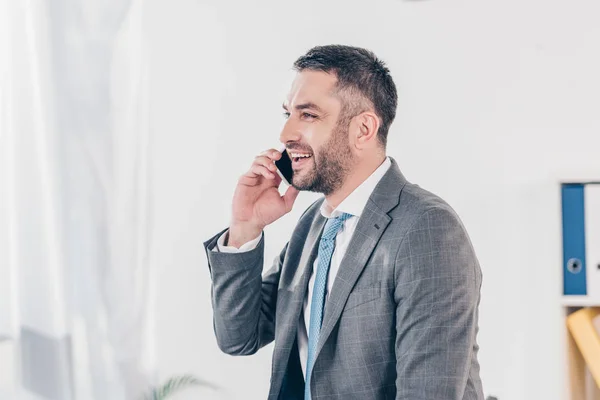 Guapo hombre de negocios sonriente en traje hablando en el teléfono inteligente en la oficina con espacio para copias - foto de stock