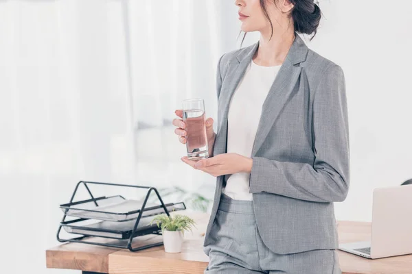 Обрезанный вид деловой женщины в костюме, держащей стакан воды в офисе — стоковое фото