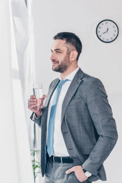 Красивий бізнесмен у костюмі тримає склянку води в офісі — стокове фото