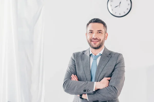 Bell'uomo d'affari sorridente in giacca e cravatta con braccia incrociate che guarda la macchina fotografica in ufficio con spazio copia — Foto stock