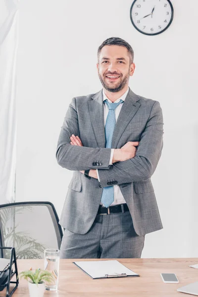 Bonito sorridente empresário em terno com cruzados braços olhando para câmera no escritório — Fotografia de Stock