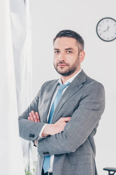 Schöner selbstbewusster Geschäftsmann im Anzug mit verschränkten Armen, der im Büro in die Kamera schaut — Stockfoto