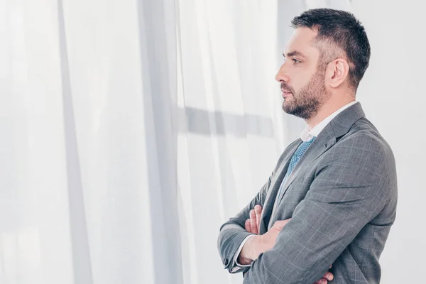 Sérieux beau homme d'affaires en costume avec les bras croisés en regardant l'espace de copie — Photo de stock