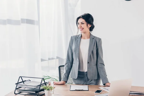 Beautiful smiling businesswoman in suit at table in office with copy space — Stock Photo