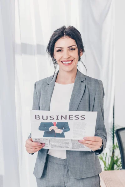 Красивая деловая женщина в костюме держит газету и смотрит в камеру в офисе — стоковое фото