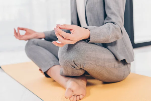Teilaufnahme einer Geschäftsfrau im Anzug, die in Lotus-Pose auf einer Fitnessmatte sitzt und im Büro meditiert — Stockfoto