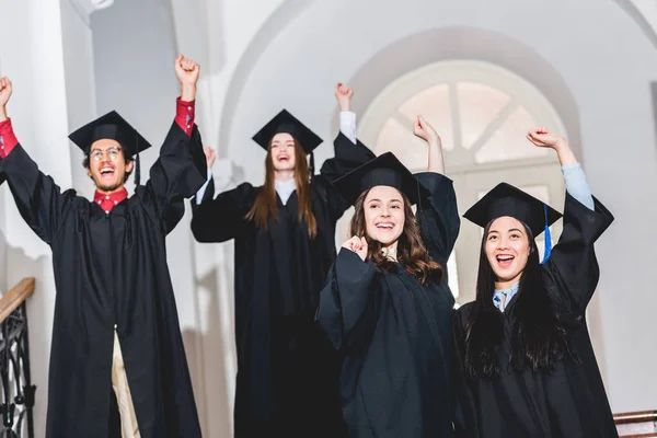 Foco seletivo de graduados universitários felizes celebrando e gesticulando na universidade — Fotografia de Stock