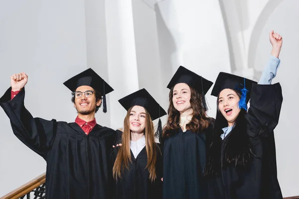 Счастливые выпускники колледжей улыбаются и жестикулируют в университете — стоковое фото
