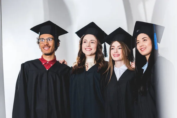 Grupo de estudiantes alegres en gorras de graduación sonriendo en la universidad - foto de stock