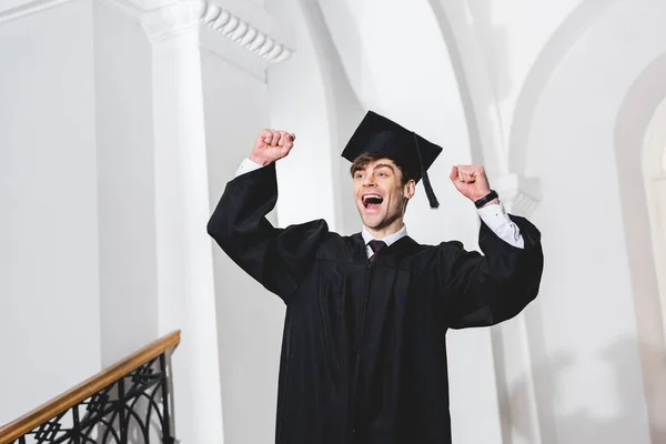 Felice giovane in berretto laurea sorridente e gesticolare all'università — Foto stock