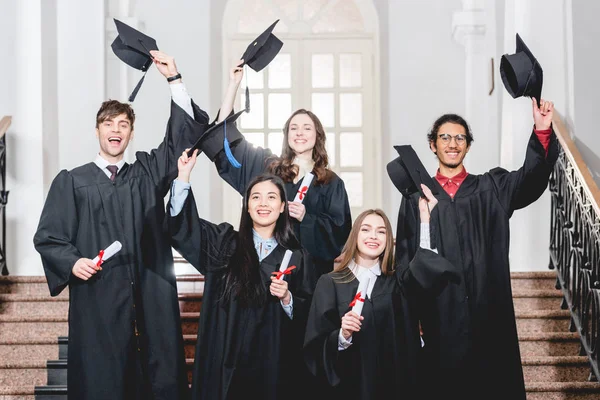 Fröhliche Gruppe von Studenten lächelt, während sie Abschlussmützen in der Hand hält — Stockfoto