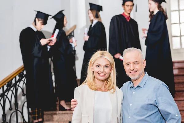 Selective focus of happy parents looking at camera near students — Stock Photo