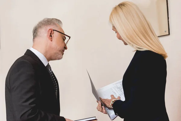 Человек в очках смотрит на папку в руках блондинки-учителя — стоковое фото