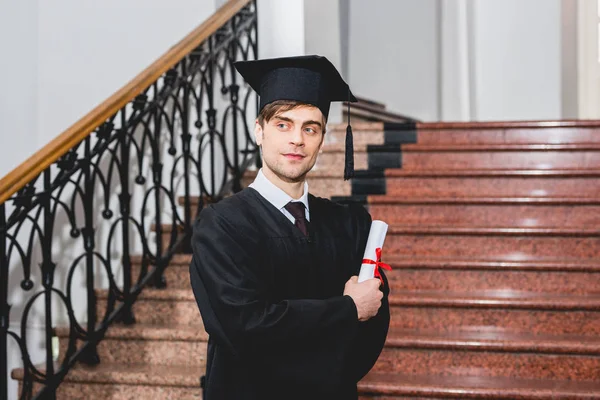 Guapo y feliz hombre en la graduación gorra de posesión de diploma en la universidad - foto de stock
