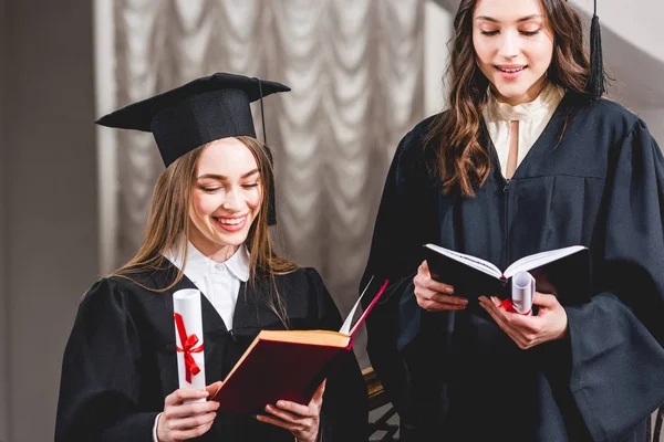 Hermosas chicas en gorras de graduación lectura de libros y la celebración de diplomas - foto de stock