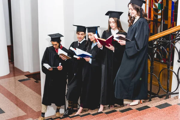 Estudiantes felices en gorras de graduación con diplomas y libros de lectura - foto de stock