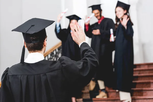 Selective focus of student in graduation cap waving hand — Stock Photo
