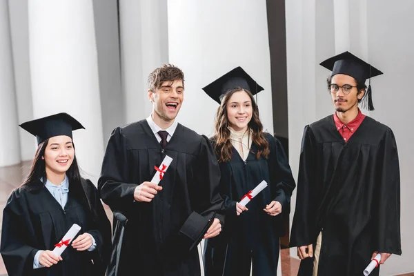 Smiling group on students in graduation gowns holding diplomas — Stock Photo