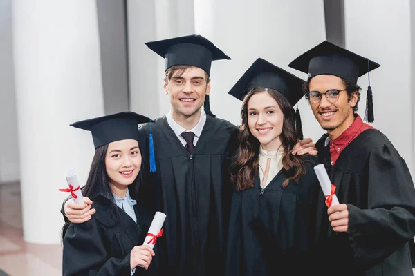 Smiling group on students looking at camera while holding diplomas — Stock Photo