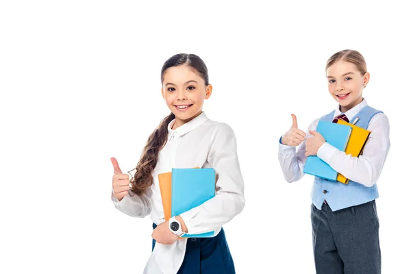 Colegialas felices en ropa formal con libros que muestran los pulgares hacia arriba aislado en blanco - foto de stock