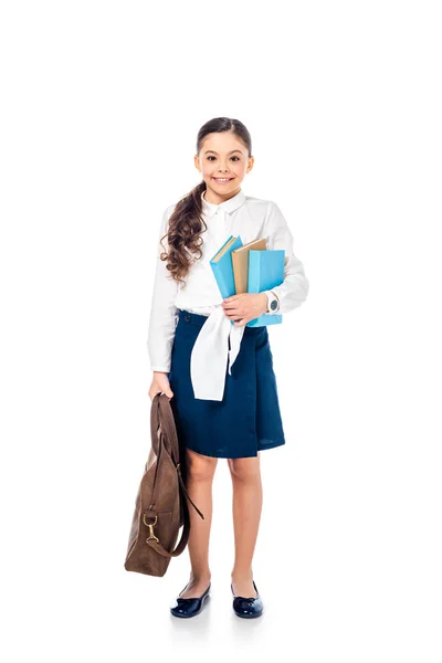 Colegiala en ropa formal mirando a la cámara y sosteniendo libros con bolsa en blanco - foto de stock