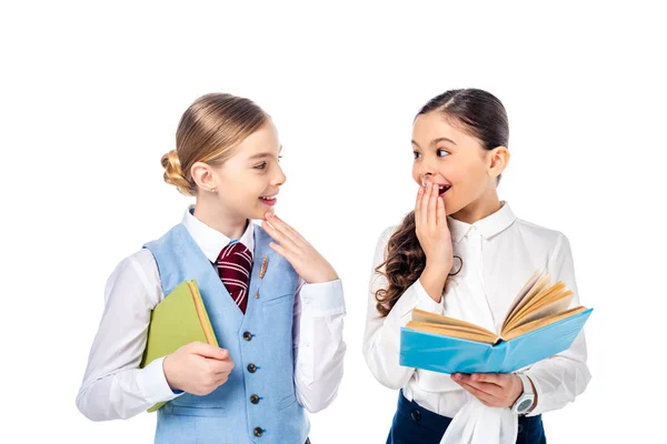 Écolières en tenue formelle avec des livres couvrant la bouche et Gesturing isolé sur blanc — Photo de stock