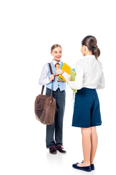 Colegialas en ropa formal con libros mirándose y hablando en blanco - foto de stock