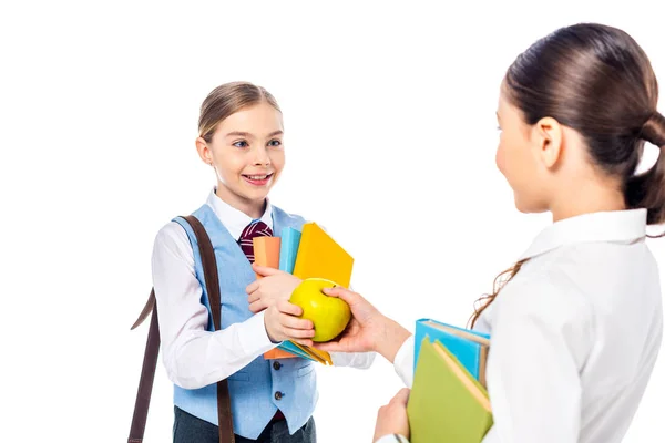 Colegialas en ropa formal con libros mirándose y compartiendo manzana aislada en blanco - foto de stock