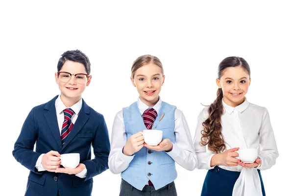 Niños de escuela felices que fingen ser empresarios con tazas de café aisladas en blanco - foto de stock