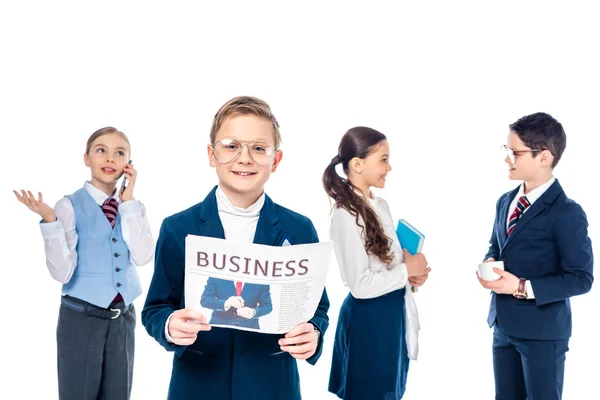 Lächelnder Schüler mit Zeitung in der Nähe von Schulkindern, die sich als Geschäftsleute auf weißem Grund ausgeben — Stockfoto