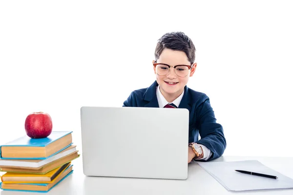 Schüler mit Brille sitzt mit Büchern am Schreibtisch und benutzt Laptop isoliert auf weiß — Stockfoto