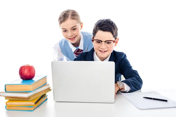 Escolares sonrientes usando el ordenador portátil en el escritorio con libros aislados en blanco - foto de stock