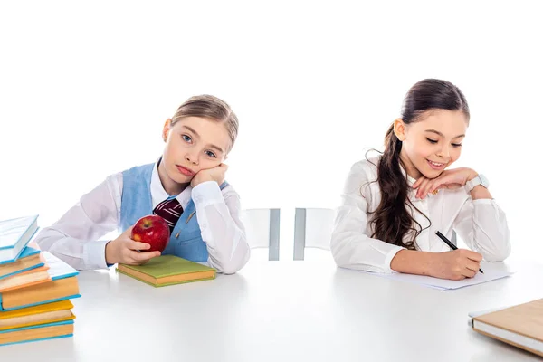 Schulmädchen in formeller Kleidung sitzen am Schreibtisch mit Büchern und schreiben isoliert auf weiß — Stockfoto