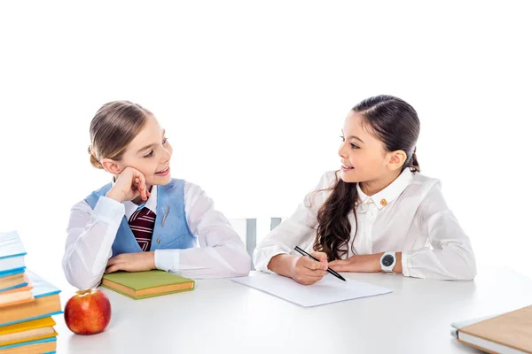 Schulmädchen in festlicher Kleidung sitzen mit Büchern am Schreibtisch und schauen sich vereinzelt auf weißem Grund an. — Stockfoto
