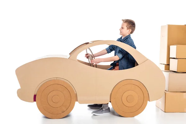 Niño sentado en el coche de cartón y sosteniendo el volante en blanco - foto de stock